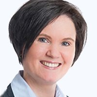 Die Frau hat ein freundliches Lächeln und strahlt Selbstbewusstsein aus, während sie in die Kamera schaut.