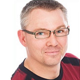 Der Mann hat eine entspannte Ausstrahlung, seine Brille betont seine Augen, während er in die Kamera schaut.