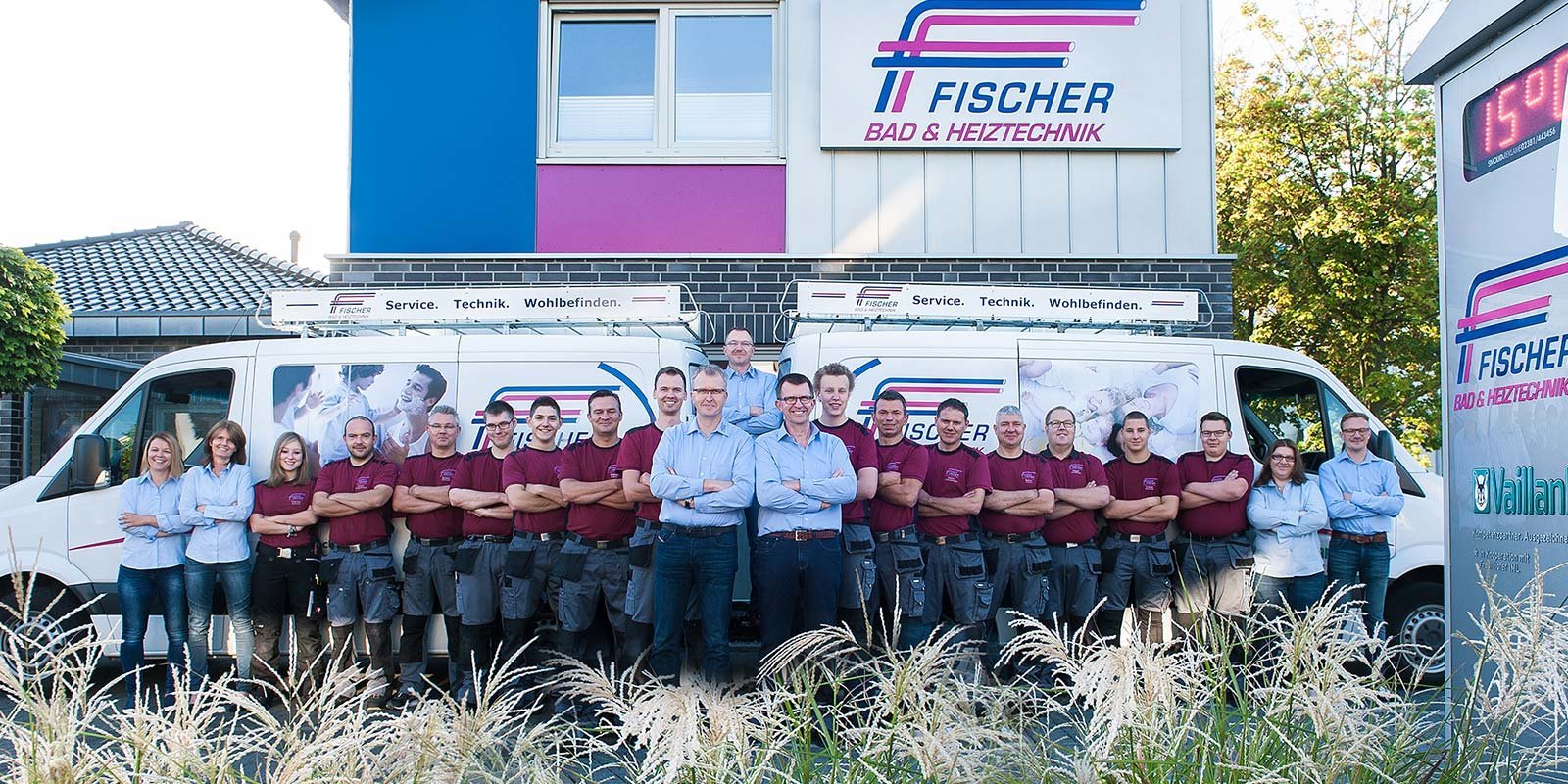 Eine Gruppe von Mitarbeitern steht stolz vor einem Firmengebäude, umgeben von grünen Pflanzen und einem Lieferwagen.