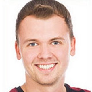 Der Mann hat ein freundliches Gesicht und trägt ein kariertes Hemd, während er direkt in die Kamera schaut.