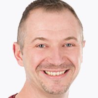 Der Mann hat ein breites Lächeln und trägt ein rotes T-Shirt, was eine positive und einladende Stimmung vermittelt.