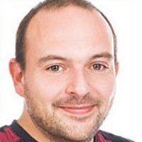 Ein lächelnder Mann mit kurzem, braunem Haar und einem gepflegten Bart, der in die Kamera schaut.
