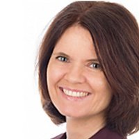 Die Frau hat eine helle Bluse an und wirkt fröhlich, während sie mit einem warmen Lächeln in die Kamera blickt.