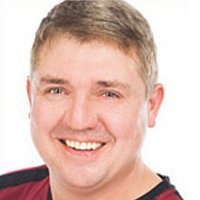 Der Mann hat ein breites Lächeln und strahlt Freude aus, während er in die Kamera schaut, mit einem hellen Hintergrund.